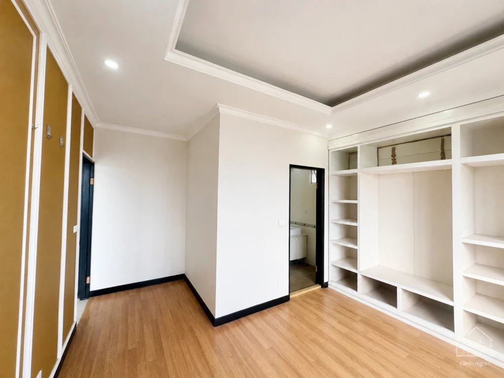 Phòng ngủ căn hộ The Flemington 96m² có tủ âm tường màu trắng, sàn gỗ và lối vào khu vệ sinh.