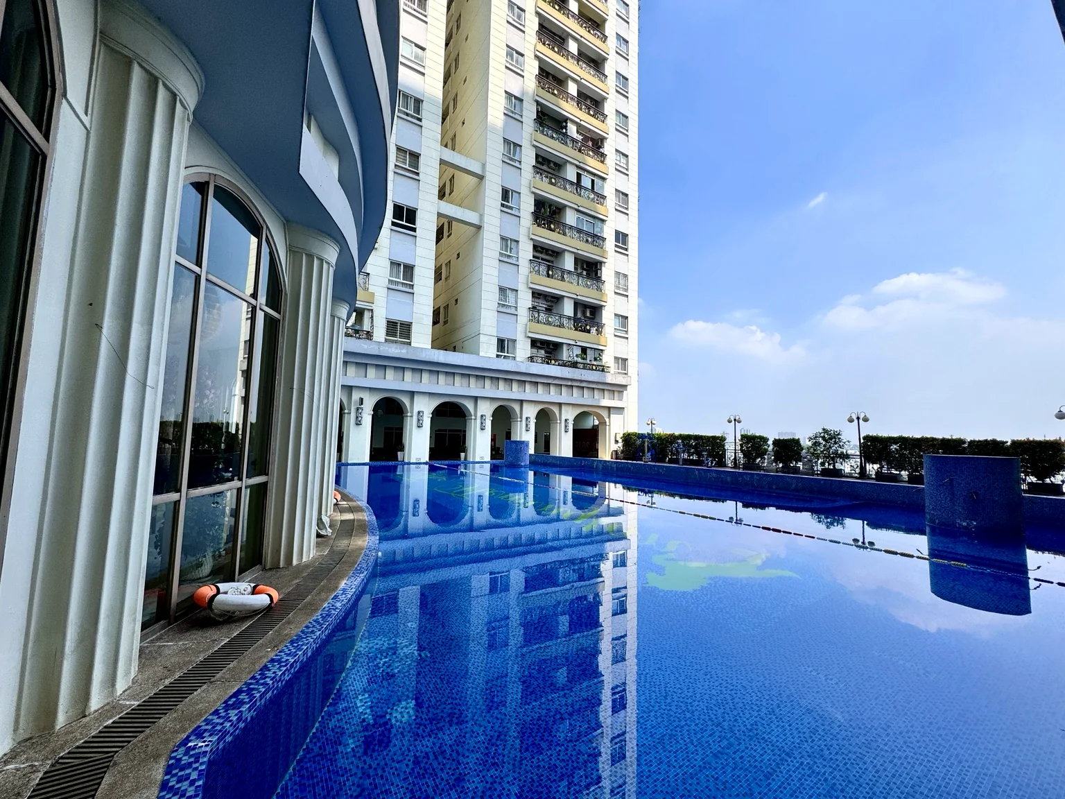 Hồ bơi The Flemington màu xanh, phản chiếu tòa nhà và bầu trời, có khu căn hộ bao quanh.