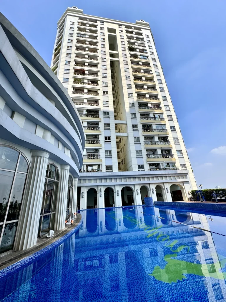 Mặt ngoài tòa nhà The Flemington cao tầng nhìn từ khu hồ bơi xanh dưới trời nắng.
