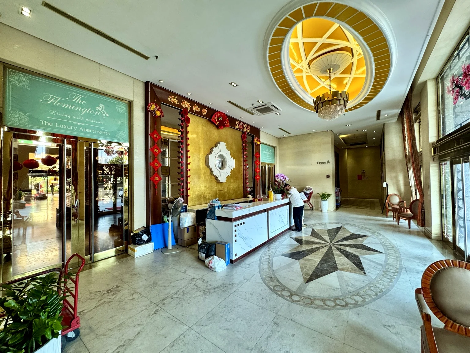Quầy lễ tân The Flemington với nền đá, trần trang trí, ghế chờ và biển The Luxury Apartments.