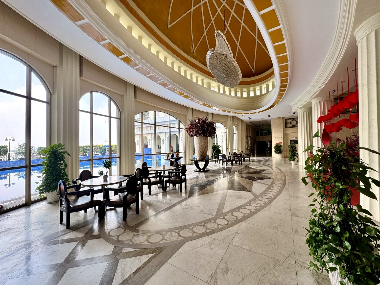 Sảnh tiện ích The Flemington với trần vòm, đèn chùm, bàn ghế tiếp khách và hồ bơi bên ngoài.