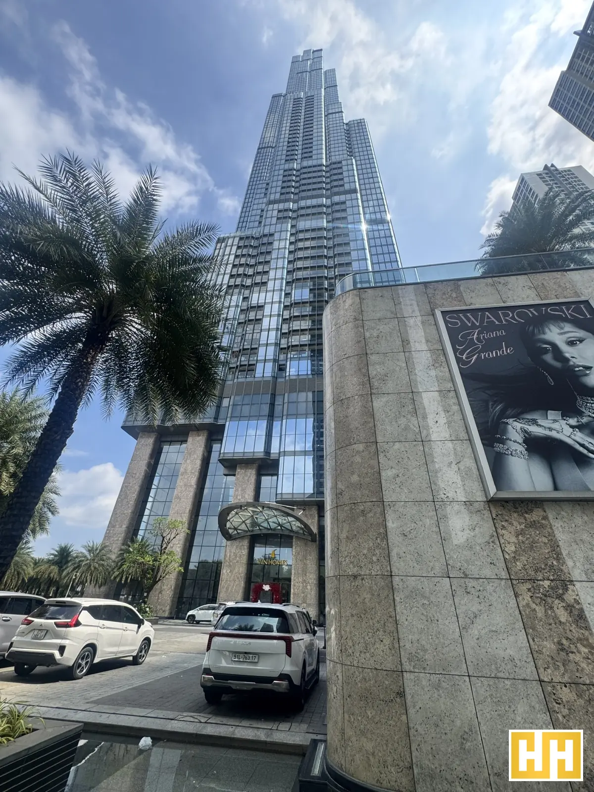Tòa Landmark 81 nhìn từ mặt đường, phía trước có hàng cây và xe ô tô.
