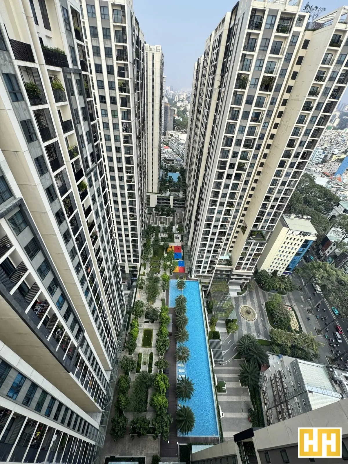 Hồ bơi dài màu xanh nằm giữa các tòa căn hộ cao tầng, nhìn từ trên xuống.