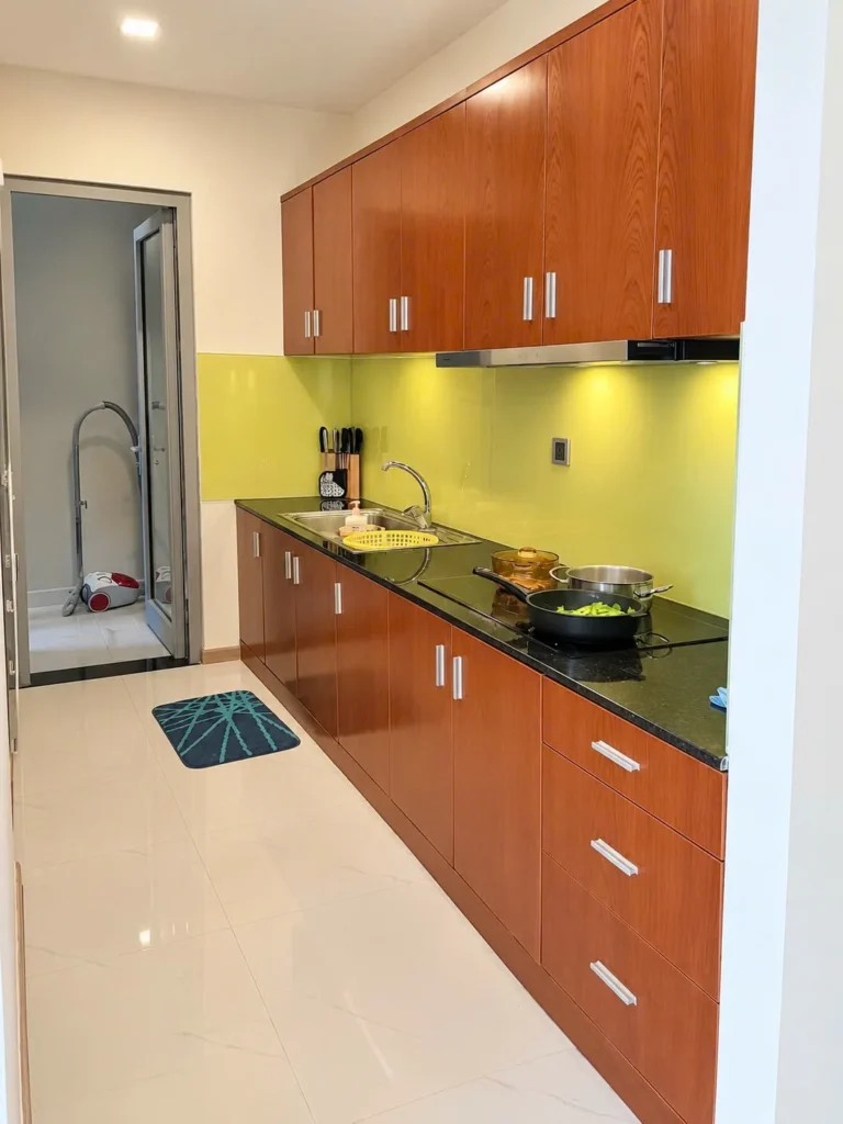 Khu bếp có tủ gỗ, mặt đá đen và kính ốp tường màu vàng