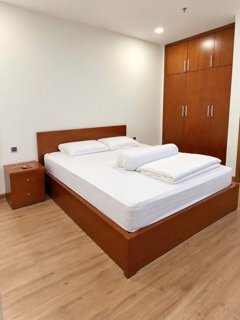 Phòng ngủ có giường gỗ, ga trắng, tủ quần áo và táp đầu giường