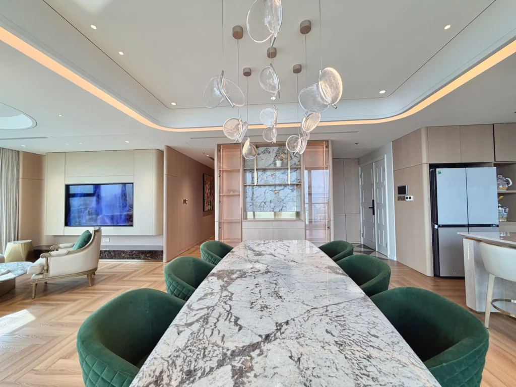 Bàn ăn dài mặt vân đá, ghế bọc xanh và đèn trang trí trong căn hộ Vinhomes Golden River.