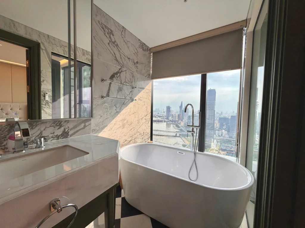 Bồn tắm độc lập cạnh cửa kính, lavabo và gương lớn trong phòng tắm căn hộ Aqua 4.