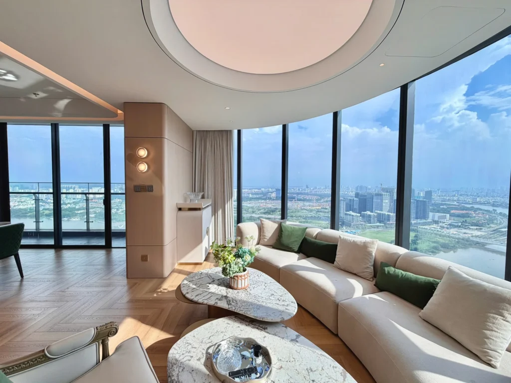 Sofa sáng màu và bàn trà trong phòng khách có cửa kính vòng cung, nhìn ra sông và thành phố.